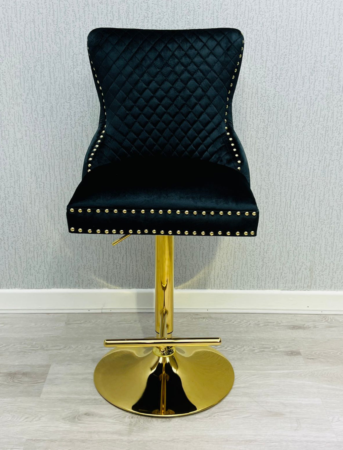 A black and gold bar stool with a tufted backrest and a gold lion knocker.