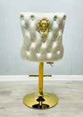 A cream colored bar stool with gold accents, featuring a tufted backrest and a lion knocker on the back.
